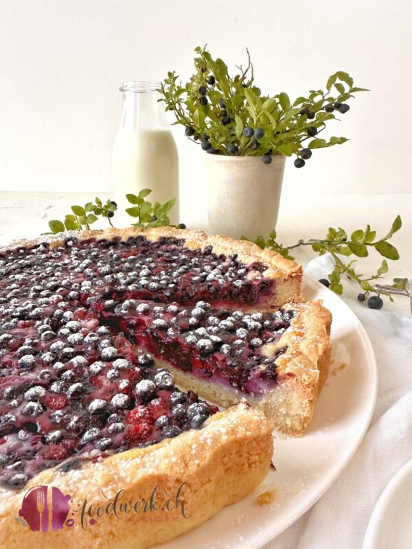 Angeschnittene Beeren Tarte mit Heidelbeerstrauch im Hintergrunde