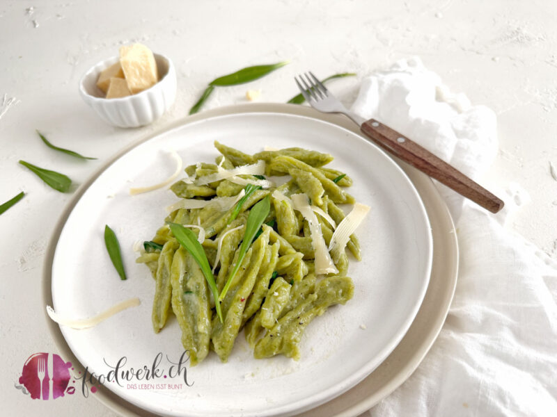 Schnelle Bärlauch- Scherennudeln 4 Portion Bärlauch Scherennudeln auf weissem Teller mit frischen Bärlauch blättern, Gabel und einer weissen Stoffserviette